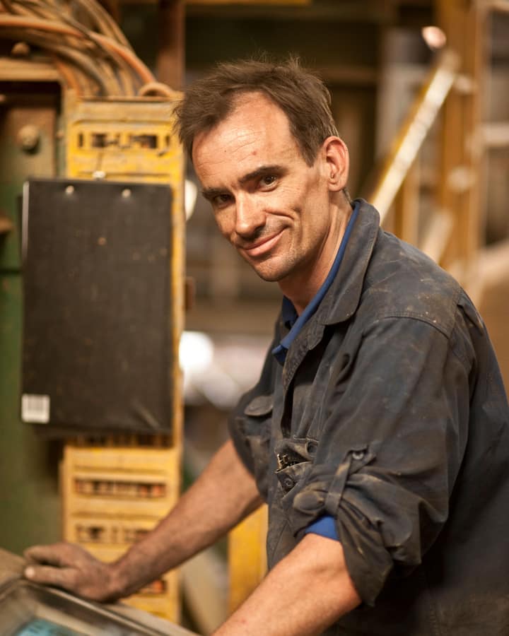 Operador sorrindo ao lado do painel de controle de uma máquina industrial